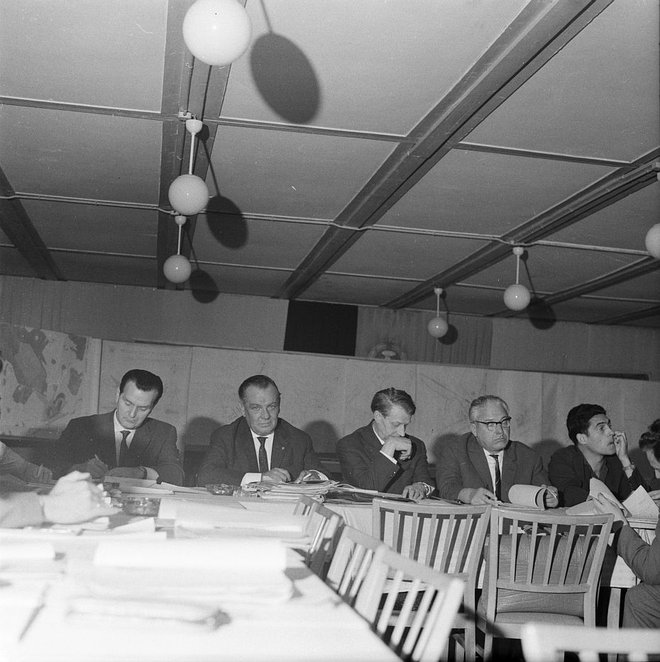 Foto: Männer sitzen an einem Tisch und beraten. Vor ihnen liegen Aktenordner.