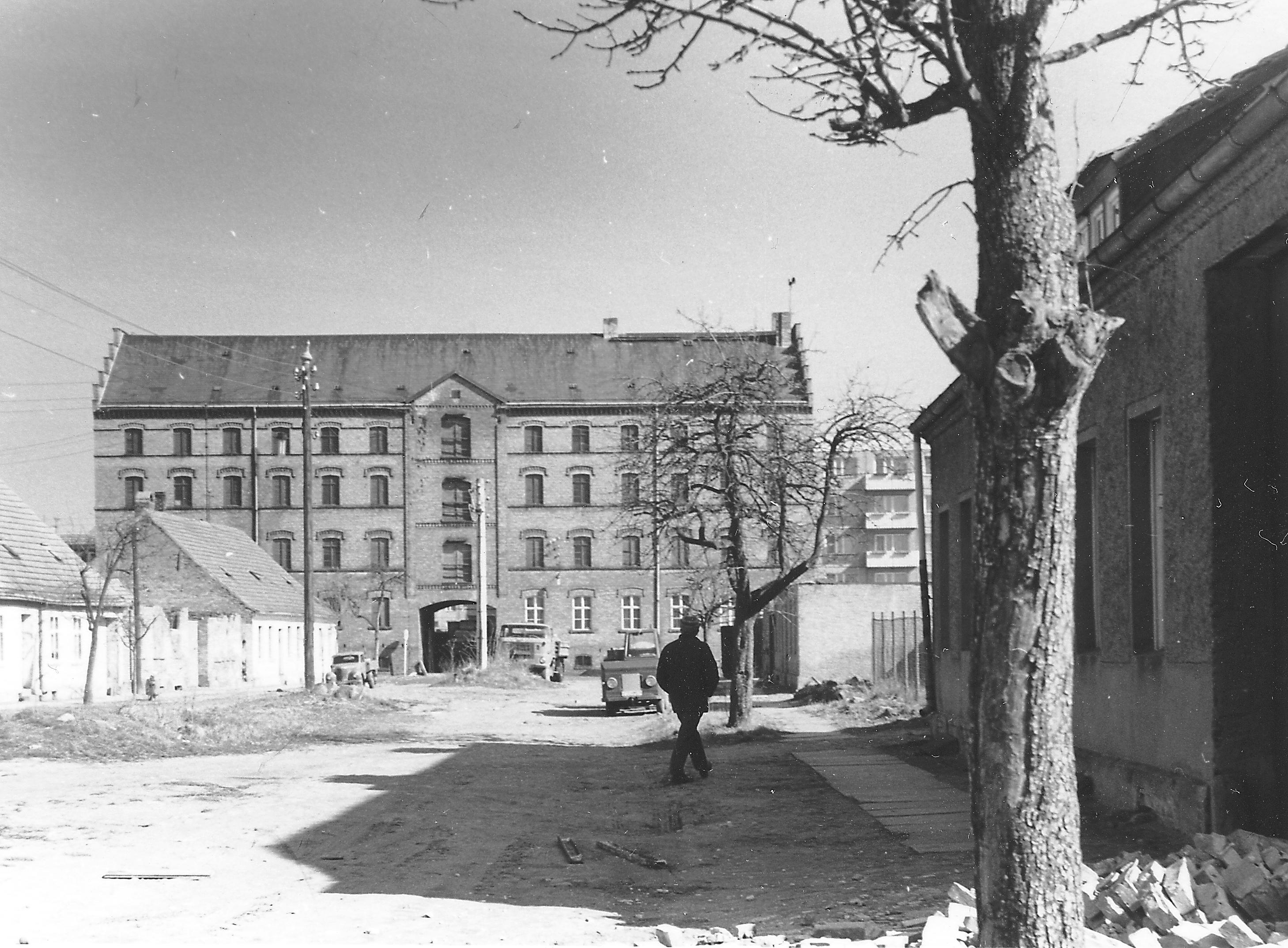 Schwarz-weiss Foto. auf dem bild ist eine Straße. An ihrem Ende steht fünfstockiges Gebeäude aus Ziegelstein.