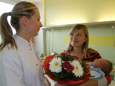 Foto: Ärztin überreicht Blumenstrauß an Mutter mit Baby