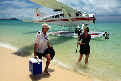 Foto: Filmerin steht im Wasser und filmt den Piloten eines Wasserflugzeugs am Strand