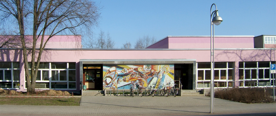 Foto: Fassade mit dem Wandbild „Kosmonaut“, Fahrradständern und Eingängen