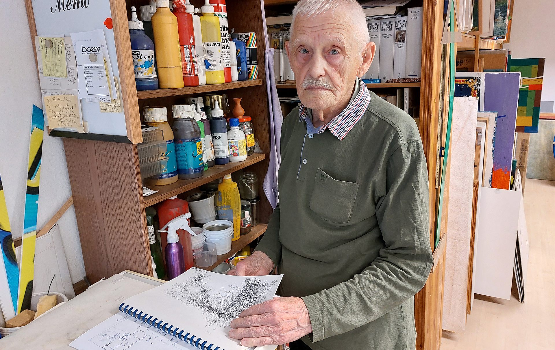 Foto: Künstler vor Regalen mit einem Skizzenblock in der Hand Foto: Künstler vor Regalen mit einem Skizzenblock in der Hand