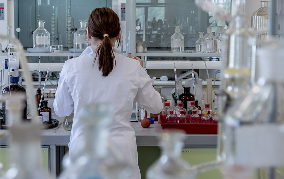 Foto: Frau mit weißem Kittel von hinten in einem Labor bei der Arbeit