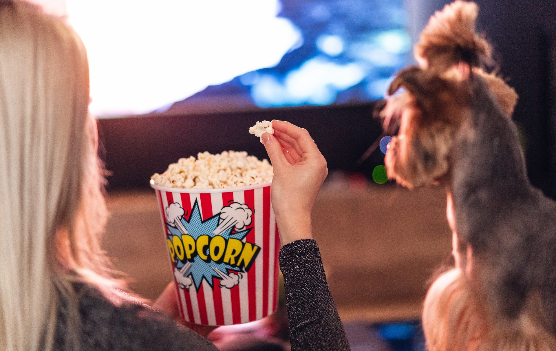 Foto: Frau mit Popcorn von hinten vor einer Leinwand, rechts ein Hund