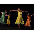 Foto: Mädchen in gelben und orangen Kleidern tanzen.