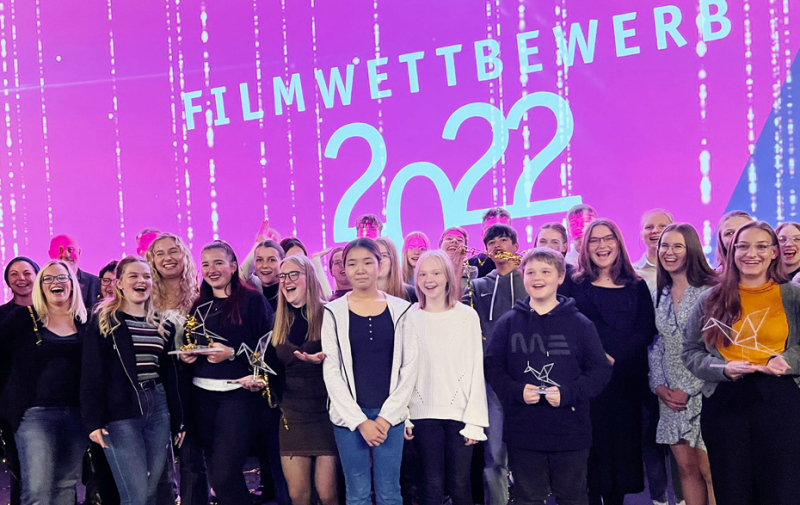 Gruppenfoto vor pinker Leinwand mit dem Text „Filmwettbewerb 2022“
