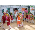 Foto: Mit buntem Haarschmuck und Kleidern kostümierte Kitakinder drehen sich in eingehackten Zweiergruppen im Kreis.